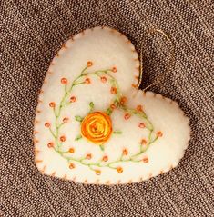 a white heart with an orange flower on it sitting on a piece of brown fabric