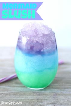 a glass filled with purple and green liquid on top of a table next to a straw