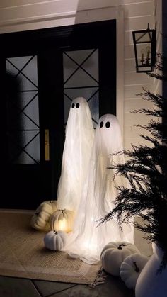 two white ghost statues sitting on top of a rug in front of a black door