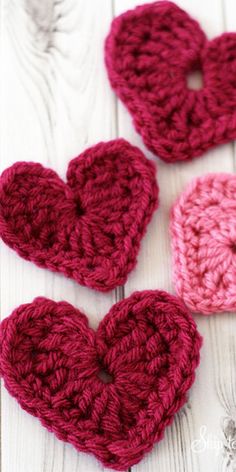 three crocheted hearts sitting on top of a white wooden table next to each other