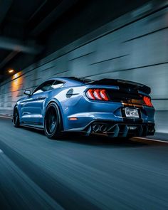 the rear end of a blue sports car driving down a street at night with its lights on