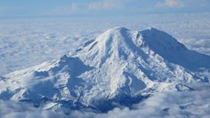 an aerial view of a snow covered mountain in the sky with clouds surrounding it and blue skies above