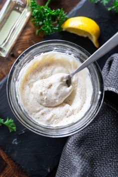 a glass bowl filled with white sauce next to a lemon and parsley