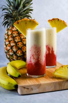 two glasses filled with fruit on top of a cutting board next to bananas and pineapples