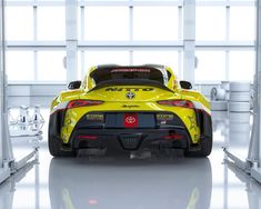 the rear end of a yellow sports car in a white room with lots of windows