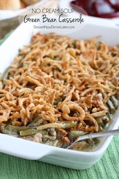 green bean casserole in a white dish with spoons and grapes on the side