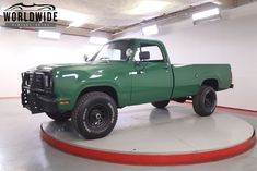 a green pick up truck is parked in a garage with red and white stripes on the floor