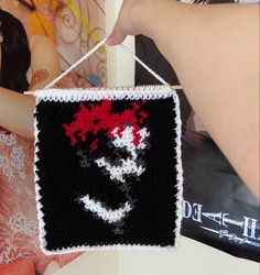 a woman holding up a black and white crocheted sign with red flowers on it