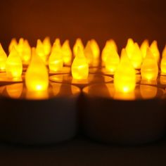 many candles are lit up in rows on a table with the light reflecting off them