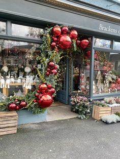 a store front with christmas decorations and wreaths on the window display in red balls