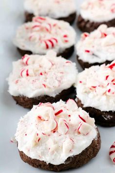 chocolate cookies with white frosting and candy canes on top sitting on a plate