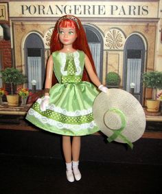 a doll with red hair wearing a green dress and holding a hat in front of a sign