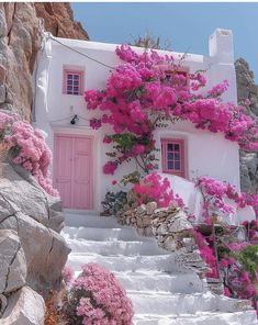 a white house with pink flowers growing on it's side and stairs leading up to the door