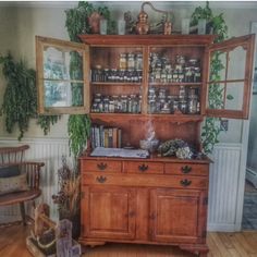 an old wooden china cabinet with many jars and herbs on it's top shelf