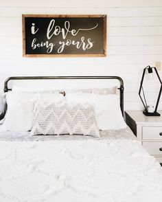 a bed with white sheets and pillows in front of a sign that says i love being yours