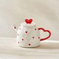 a teapot with hearts painted on it sitting on a white tablecloth next to a wall