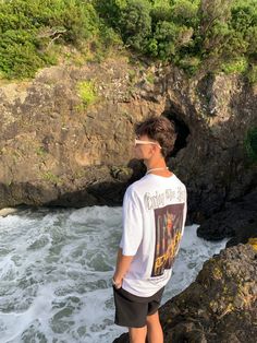 a man standing on top of a rock next to the ocean