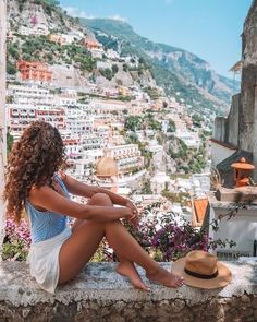 a woman is sitting on a ledge overlooking the city