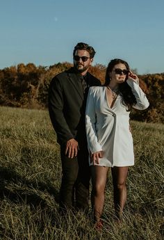 a man and woman are standing in the tall grass together, one is wearing sunglasses