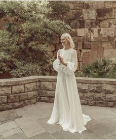 a woman in a white dress standing on a stone wall