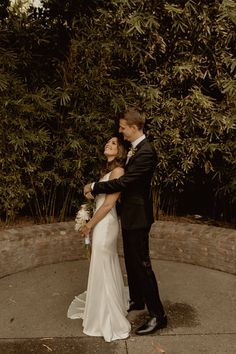 a bride and groom standing in front of some trees