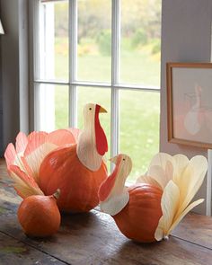 two pumpkins sitting on top of a wooden table next to a fake turkey in front of a window