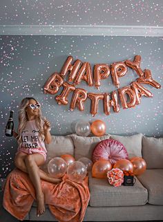 a woman sitting on top of a couch next to balloons that say happy birthday in front of her