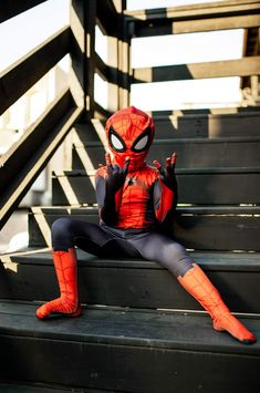 a young boy dressed as spider - man sitting on some stairs