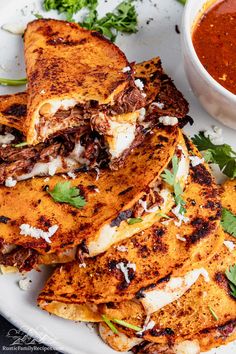 a white plate topped with quesadillas next to a bowl of chili sauce