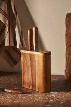 a wooden box with two knives in it on a table next to a towel rack