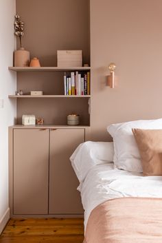 a bed with white sheets and pillows in a bedroom next to a book shelf filled with books