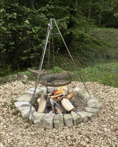 an outdoor fire pit with logs in it and a metal frame on the top, surrounded by leaves