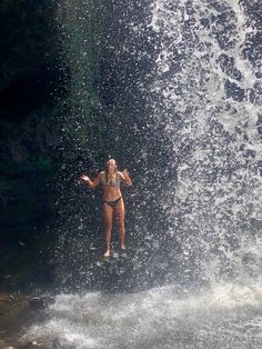 a woman standing in the middle of a waterfall while holding on to her arms as she jumps into the water