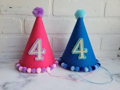 two felt birthday hats with the number four on them and pom - poms