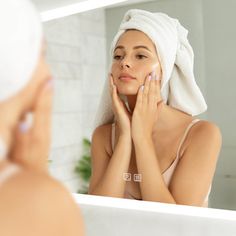 a woman with a towel on her head is looking at her face in the mirror