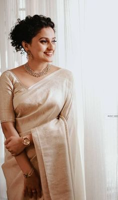 a woman in a beige sari standing next to a window with her hands on her hips