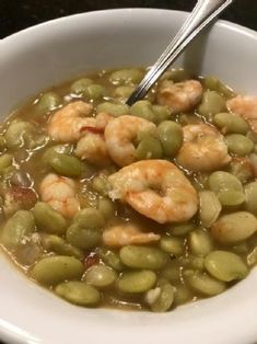 a white bowl filled with green beans and shrimp next to a silver spoon on top of a table