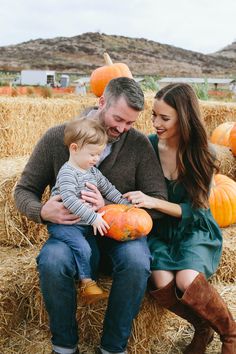 a man, woman and child sitting on hay bales with pumpkins