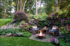 a fire pit in the middle of a garden surrounded by flowers and trees, with chairs around it