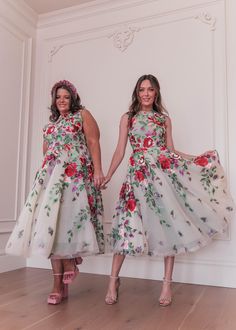 two women standing next to each other holding hands and wearing dresses with flowers on them