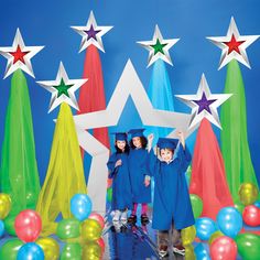 three children in graduation gowns standing under stars and balloons