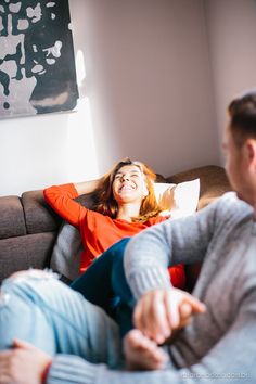 two people sitting on a couch laughing and pointing at something in the air above them