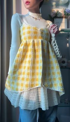 a woman wearing a yellow and white dress standing in front of a window with her hands on her hips