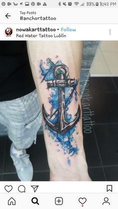 an anchor tattoo on the arm with blue ink and watercolor splatters around it