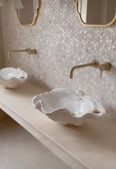 two white bowls sitting on top of a counter in a bathroom next to mirrors and sinks