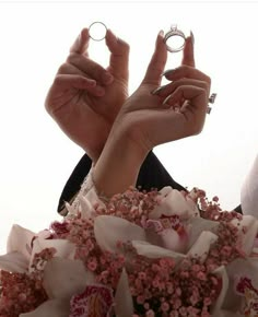 two hands holding wedding rings in front of the camera with pink flowers on it and white background