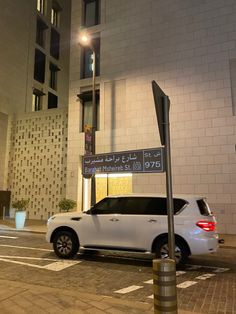 a white car parked in front of a tall building at night with arabic writing on it