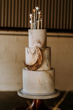 a three tiered white cake with gold stars and moon decorations on it's side