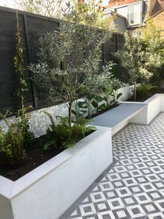 an outdoor garden with trees and plants in the center, on a tiled floor next to a fence