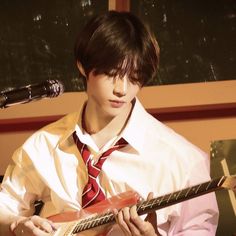 a young man wearing a tie and holding a guitar in front of a microphone,